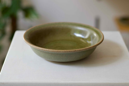 Green ceramic bowl on a white surface with a blurred background