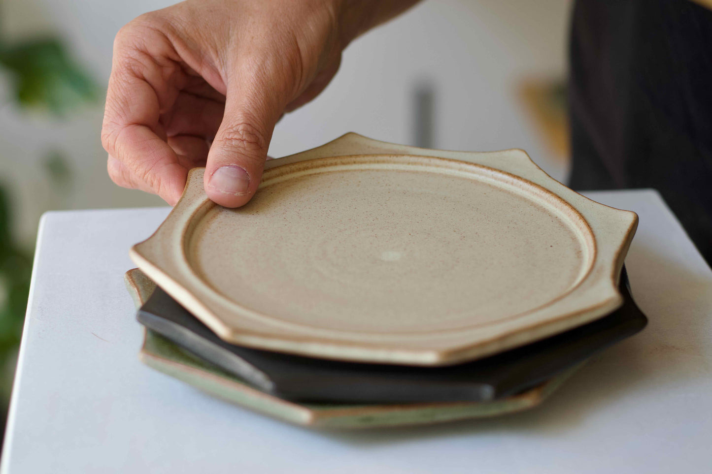 Person holding a stack of ceramic plates on a white surface