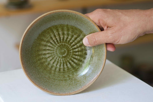 Hand holding a green ceramic plate with a textured design on a white surface.