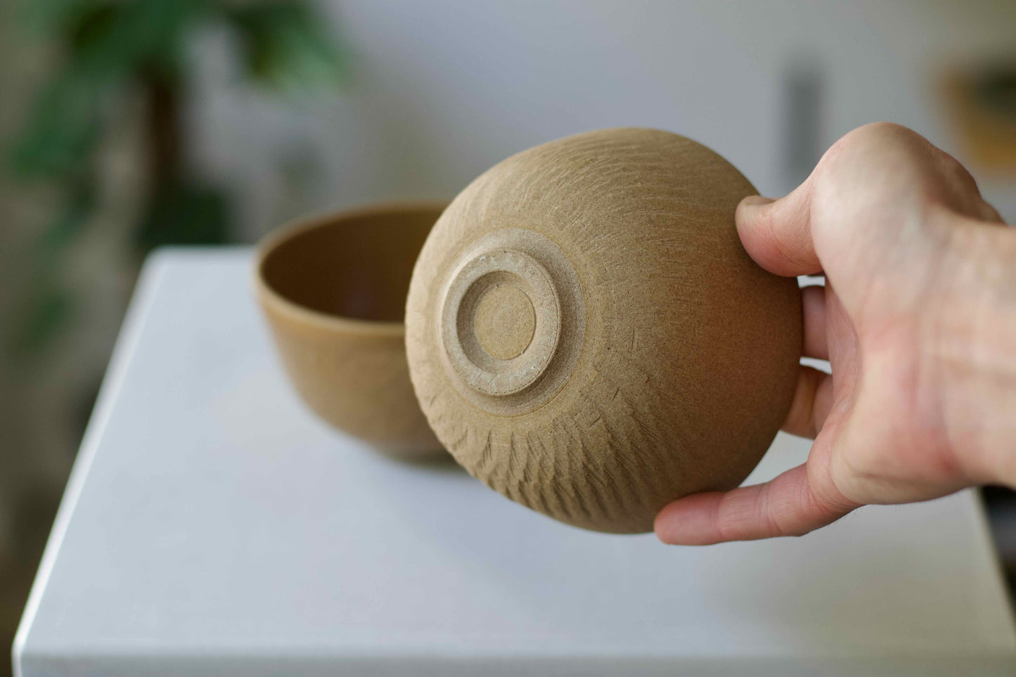 Hand holding a textured ceramic bowl on a white surface with a blurred background