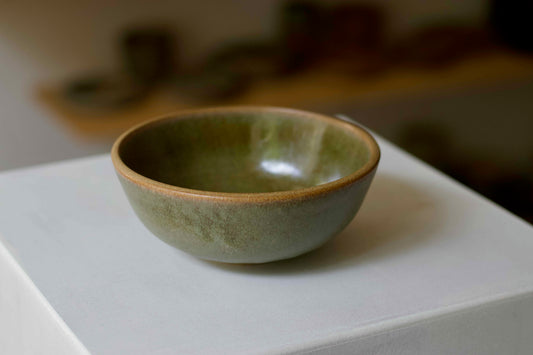 Green ceramic bowl on a white surface with a blurred background