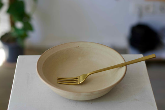 Beige bowl with a gold fork on a white surface, blurred background