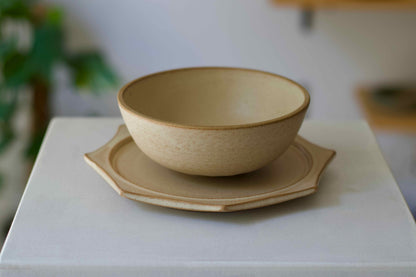 Beige ceramic bowl and plate set on a white surface with a blurred background