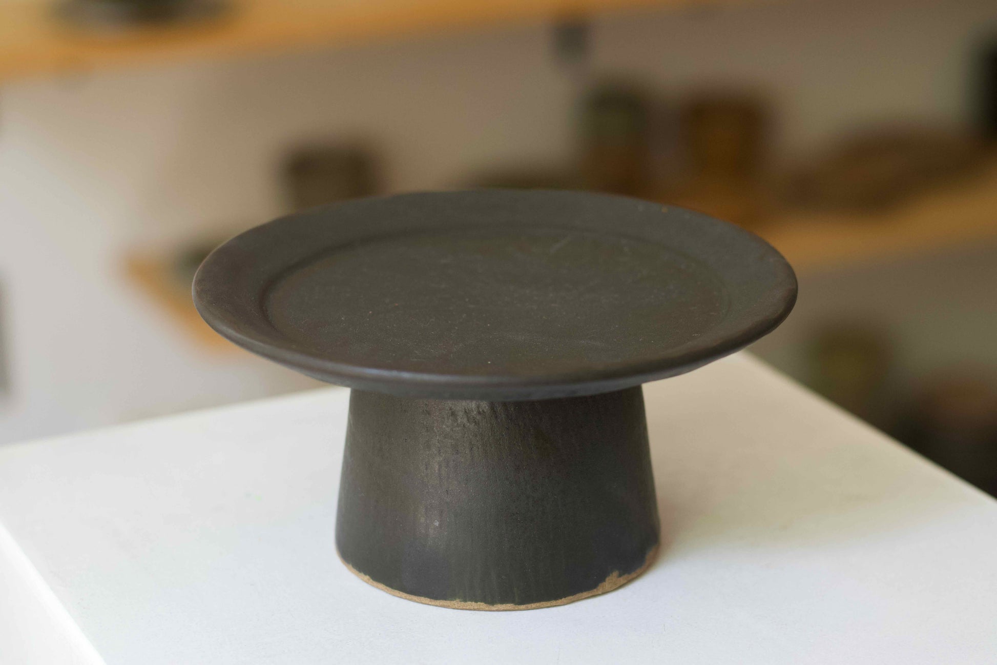 Black ceramic cake stand on a white surface with a blurred background