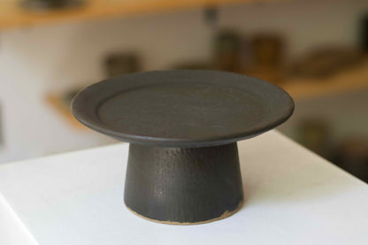 Black ceramic cake stand on a white surface with a blurred background