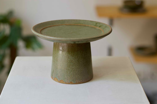 Green ceramic pedestal on a white surface with a blurred background
