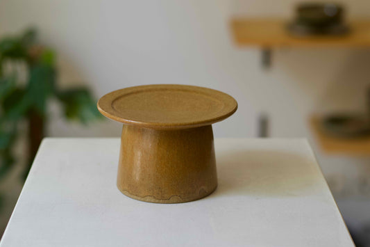 Brown ceramic pedestal on a white surface with a blurred background