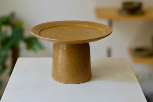 Brown ceramic pedestal dish on a white surface with a blurred background