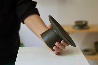 Person holding a ceramic pedestal with a blurred background