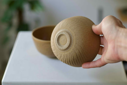 Hand holding a textured ceramic bowl on a white surface with a blurred background